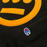 Detailed close up of black hoodie with yellow Hieroglyphics hip-hop logo on the chest and Champion logo on the sleeve.