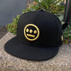 Black New Era cap with gold embroidered Hieroglyphics hip-hop logo on the crown outside in natural lighting.